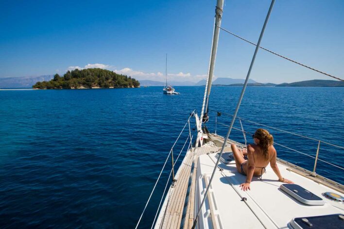 Woman sits on front of yacht in sunshine