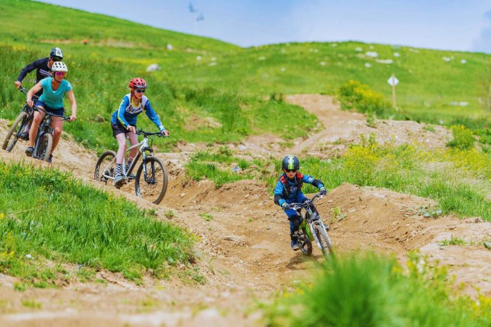 A family go down a mountain bike trail in the French Alps on a sunny day