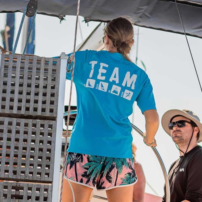 Girl stands at helm of yacht. Two men sit either side of the cockpit