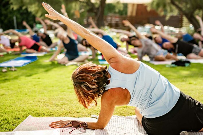 A woman leads a yoga class, stretching up to her left
