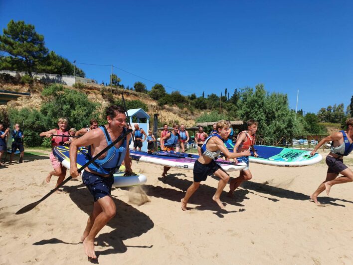 A family run down to the water edge carrying surfboards and paddles