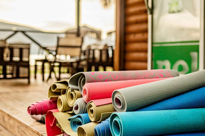Pile of rolled up yoga mats in different colours. Beach bar chairs, beach and sea in the background