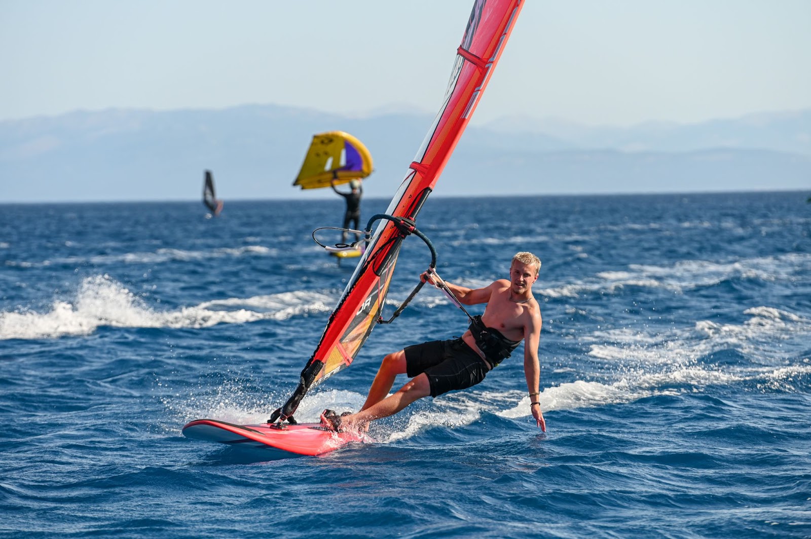 windsurfer dragging their hand in the water in a flat bay with wingfoilers behind