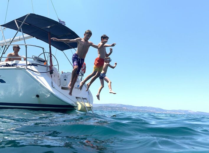 Three children jump off the back of a white sailing yacht into the sea