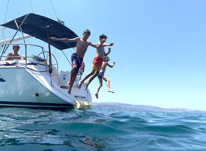 3 children jump off the back of a yacht on a sailing holiday in Greece