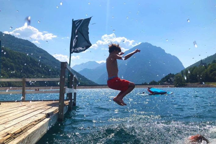 boy jumping in an alpine lake in the summer with watersports in the background and other activity sports