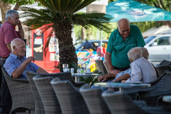 Older men sat conversing around restaurant table in Lixouri Square, Kefalonia