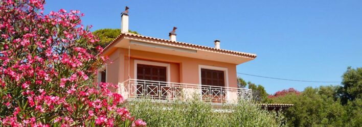 Greek style beach house with balcony beside large pink blossom tree