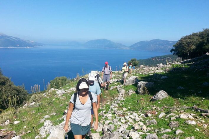 A line of walking tourists explore a coastal trail in the sunshine