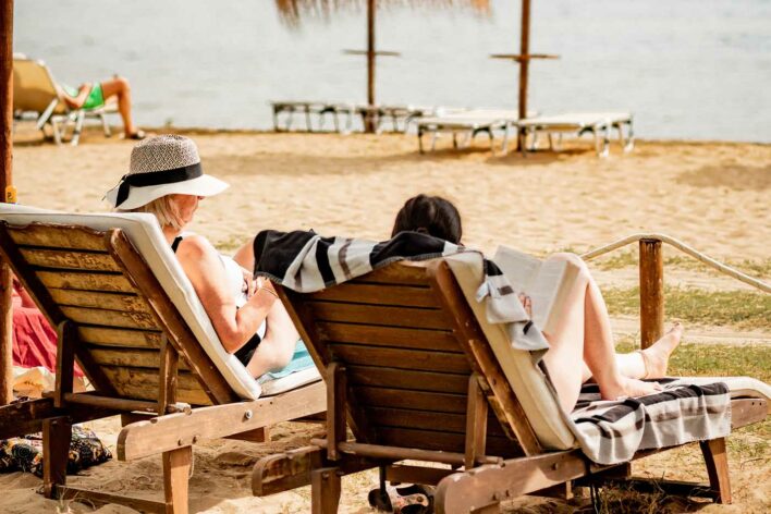 Two people sit sun loungers on a beach. Both people are reading books