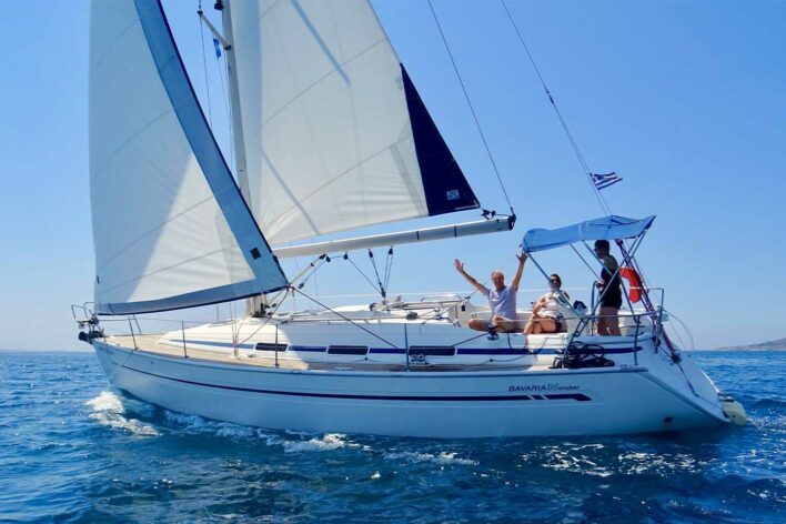 Man, woman and two teenagers sailing on a yacht in Greece. The yacht has sails up and is sailing along.